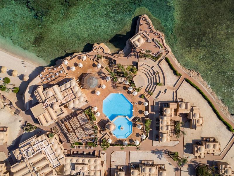 Vista aérea de un hotel con piscina junto a la playa y agua de mar clara.