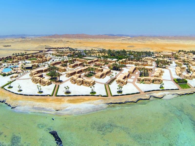 Resort en isla con edificios blancos y agua turquesa en un paisaje desértico.