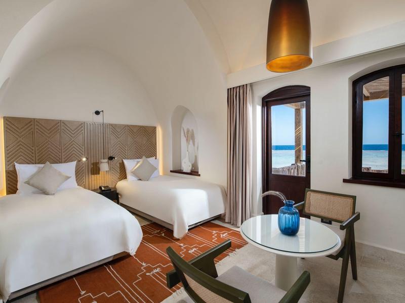 Habitación moderna con dos camas, mesa, sillas y vista al mar a través de las ventanas.