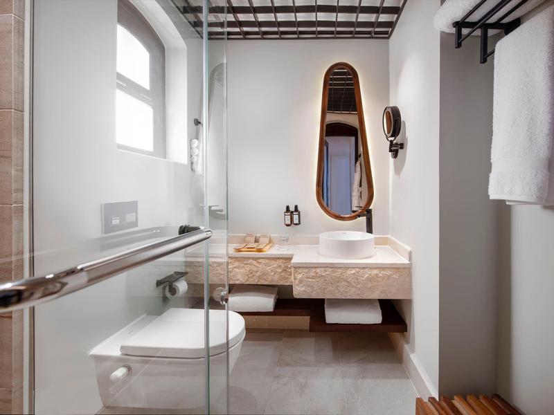 Baño moderno con ducha, inodoro, lavabo y grandes ventanas en tonos neutros.