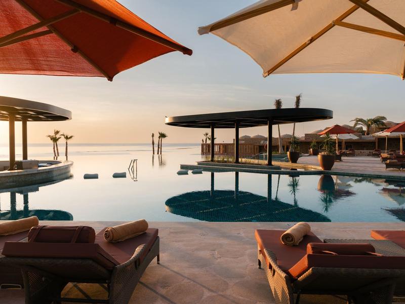 Una tranquila zona de piscina con tumbonas y sombrillas al atardecer junto al mar.