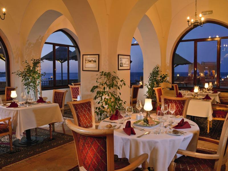 Restaurante elegante con mesas vestidas y grandes ventanales arqueados con vista al agua.