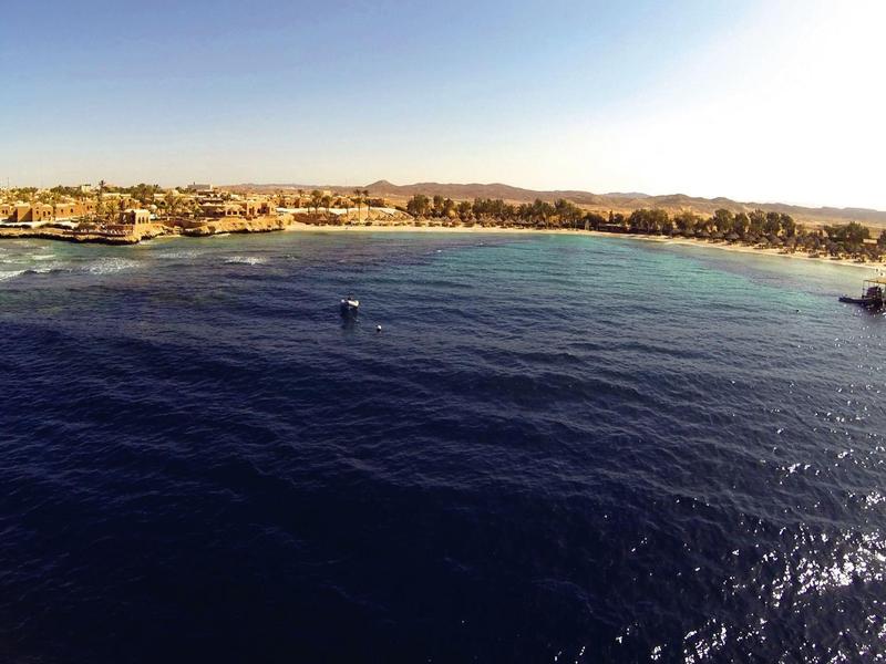 Vista panorámica de una playa con agua azul clara y un bote bajo un cielo soleado.