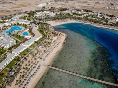 Veduta aerea di un resort sulla spiaggia con piscine, lettini e acqua azzurra limpida.