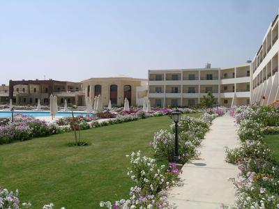 Complesso alberghiero con piscina, giardino curato e fiori in fiore sotto un cielo azzurro.