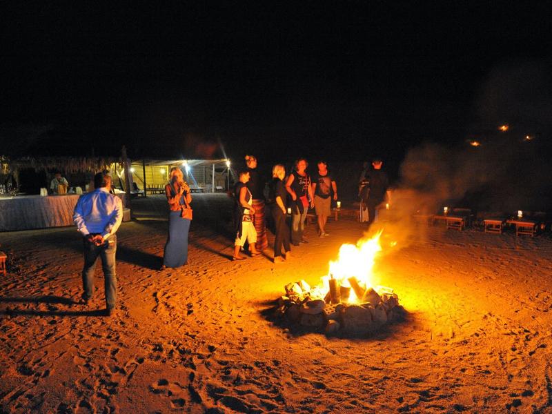 Gruppo di persone intorno a un falò sulla spiaggia di notte.
