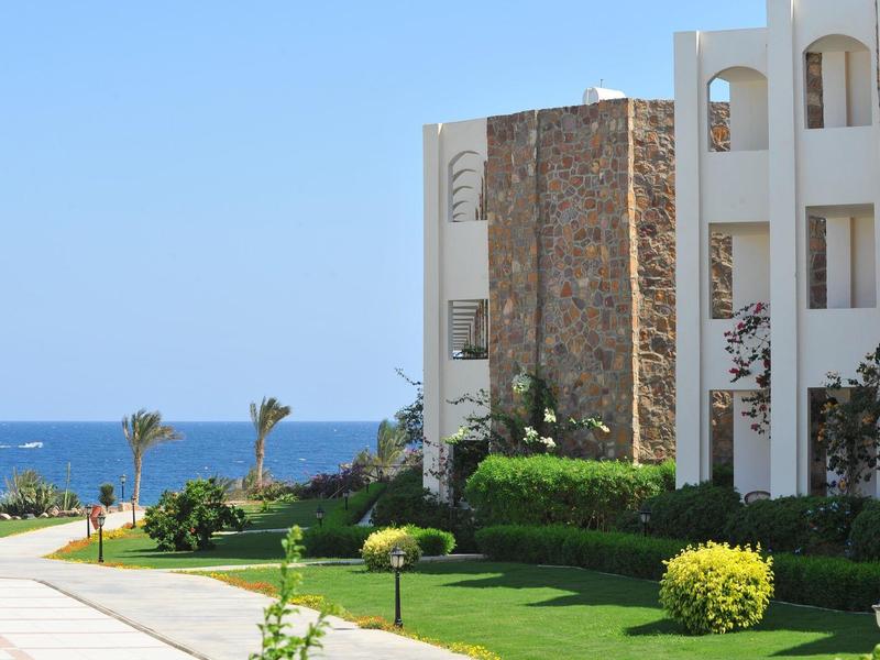 Complesso alberghiero moderno su più piani con giardini e vista sul mare sotto un cielo sereno.
