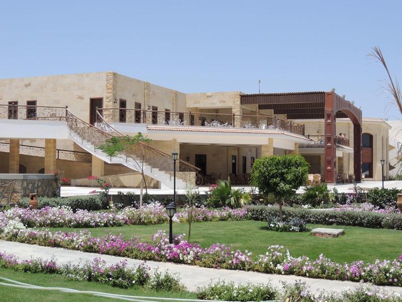 Edificio alberghiero moderno con giardino piantumato e aiuole fiorite in primo piano.