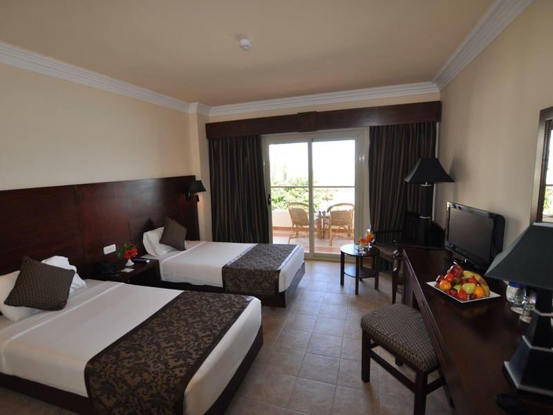 Camera d'hotel con due letti singoli, scrivania e balcone con vista sul verde.