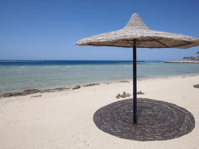 Un ombrellone di paglia solitario su una spiaggia di sabbia vuota con cielo azzurro.