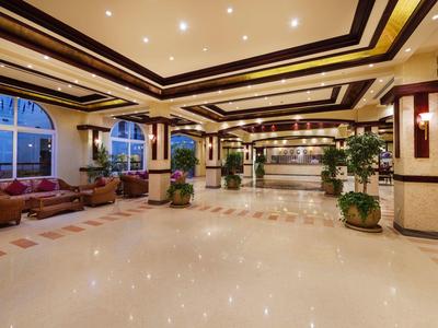 Großer, heller Hotellobby-Bereich mit poliertem Boden, Sofas, Pflanzen und aufwendig gestaltetem Deckenlicht.
