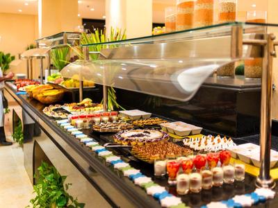 Buffet mit verschiedenen Desserts und Kuchen, bunte Auswahl auf schwarzer Theke, Kellner im Hintergrund.