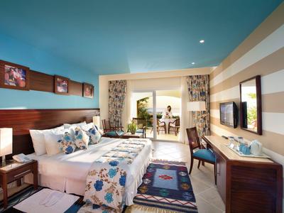 Modernes Hotelzimmer mit großem Bett, buntem Bettbezug, Schreibtisch und Balkon mit Sitzgelegenheit.