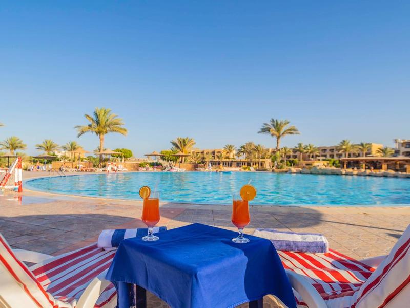 Strefa basenowa z leżakami, niebieskim obrusem i widokiem na palmy i czyste niebo.