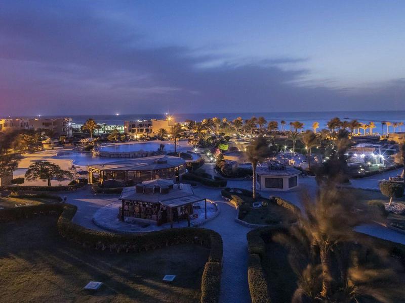 Widok na oświetlone miejsce wypoczynkowe z bungalowami i palmami o zmierzchu.