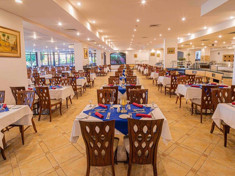 Duża, dobrze oświetlona jadalnia z wieloma schludnie nakrytymi stołami i krzesłami.