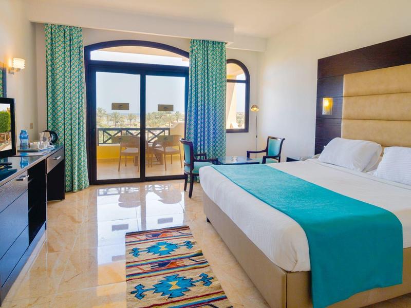 Jasny pokój hotelowy z łóżkiem podwójnym, balkonem i widokiem na morze.