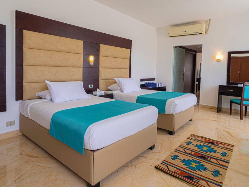 Nowoczesny pokój hotelowy z dwoma łóżkami, klimatyzacją, kolorowym dywanem i biurkiem.