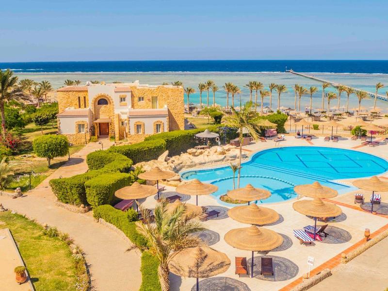 Widok na ośrodek z basenem, parasolami i widokiem na morze w słoneczny dzień.