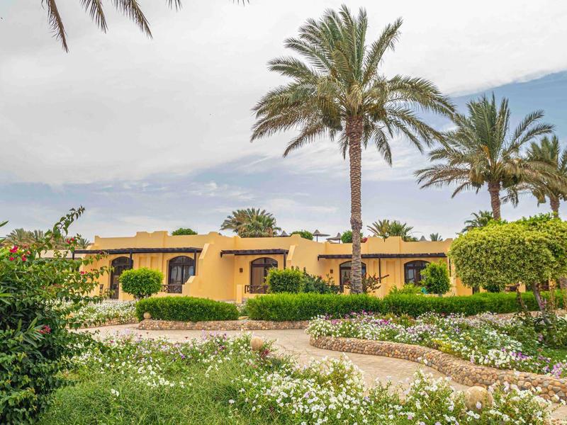 Ośrodek hotelowy z żółtymi bungalowami, palmami i zadbanymi ogrodami pod pochmurnym niebem