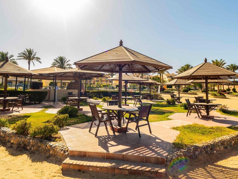 Słoneczny taras hotelowy z stołami, krzesłami i parasolami w tropikalnym otoczeniu.