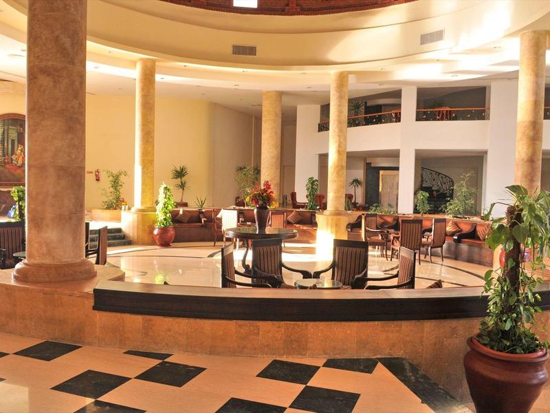 Jasny hol hotelowy z kolumnami, miejscami do siedzenia i centralną fontanną.