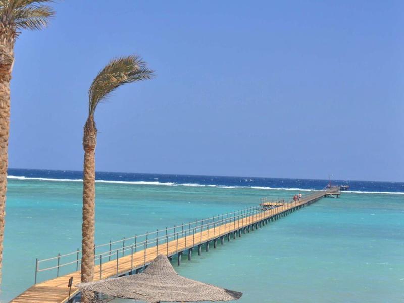 Drewniany pomost rozciąga się nad turkusowym morzem z palmami na pierwszym planie.