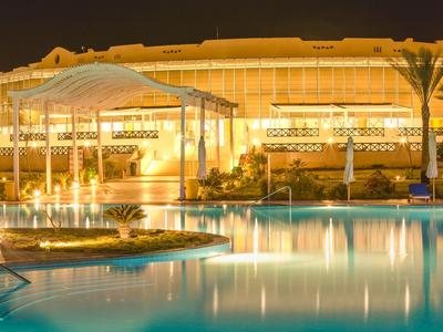 Illuminated hotel pool with pavilion and palm trees at night