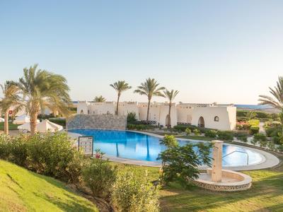Swimming pool in tropical garden setting with palm trees and white building in background.