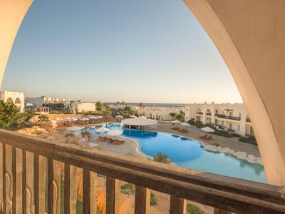 View from a balcony overlooking a pool and hotel buildings under clear sky.