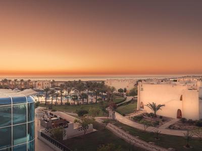 View of a hotel area with pool and palm trees at sunset by the sea.