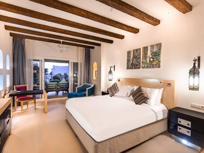 Chambre d'hôtel élégante avec lit double, murs blancs, poutres en bois et vue sur la terrasse.