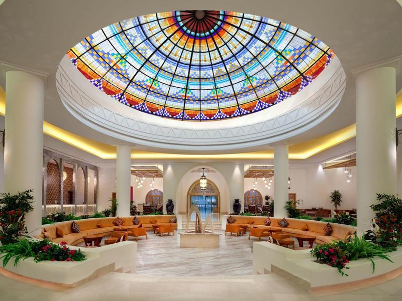 Lobby d'hôtel spacieux avec un grand dôme en vitrail coloré au plafond.