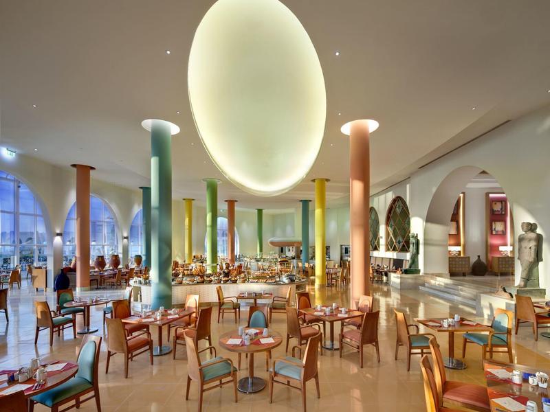 Grand restaurant lumineux avec colonnes colorées et chaises en bois autour des tables