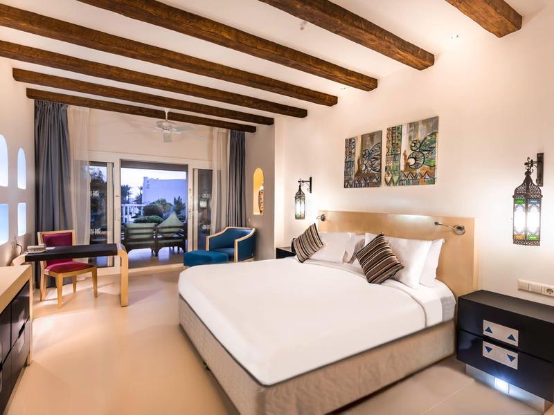 Chambre d'hôtel élégante avec lit double, murs blancs, poutres en bois et vue sur la terrasse.