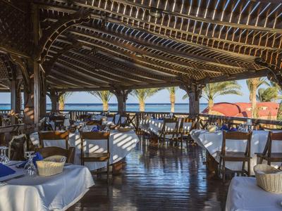 Restaurant en plein air avec sol en bois et vue sur la mer sous une zone couverte.
