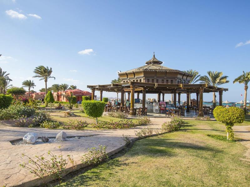 Un pavillon dans un jardin bien entretenu avec des palmiers sous un ciel bleu.