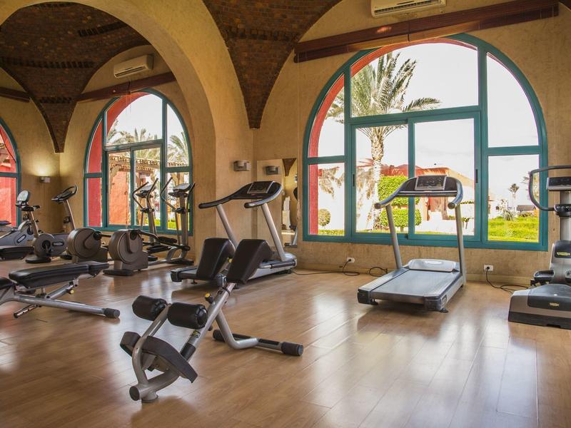 Salle de sport lumineuse avec grandes fenêtres arquées et équipements modernes.