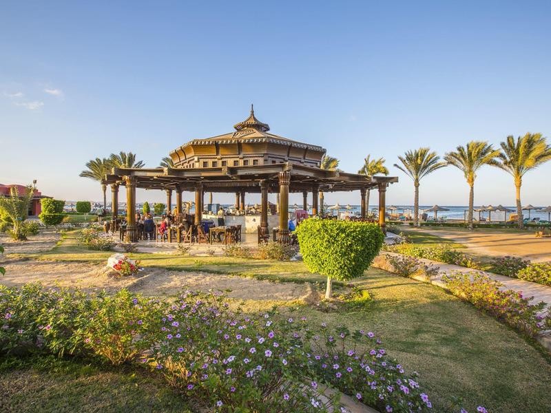 Un pavillon dans un jardin bien entretenu avec des palmiers sous un ciel bleu.