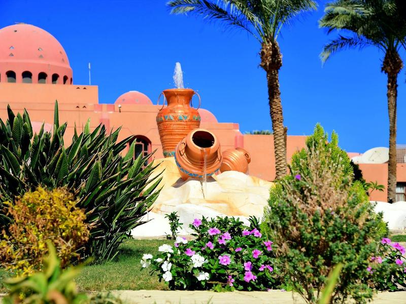 Jardin d'hôtel avec des palmiers, des plantes en fleurs et un grand élément décoratif sous un ciel bleu