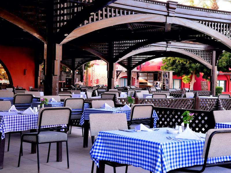 Espace extérieur vide d'un restaurant avec nappes à carreaux bleus et blancs et chaises sous un abri.