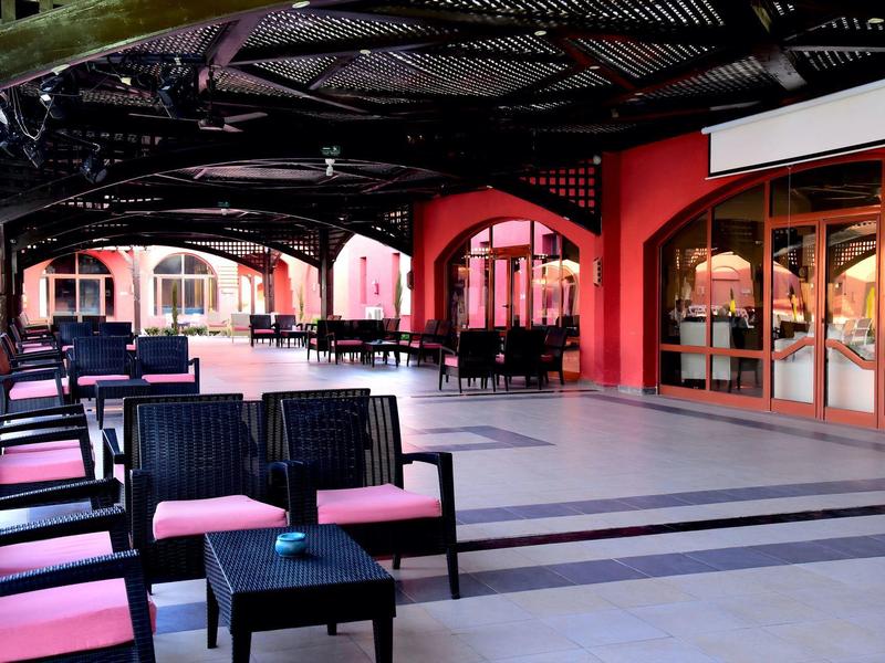 Terrasse couverte avec des sièges et des tables devant un restaurant aux murs rouges.