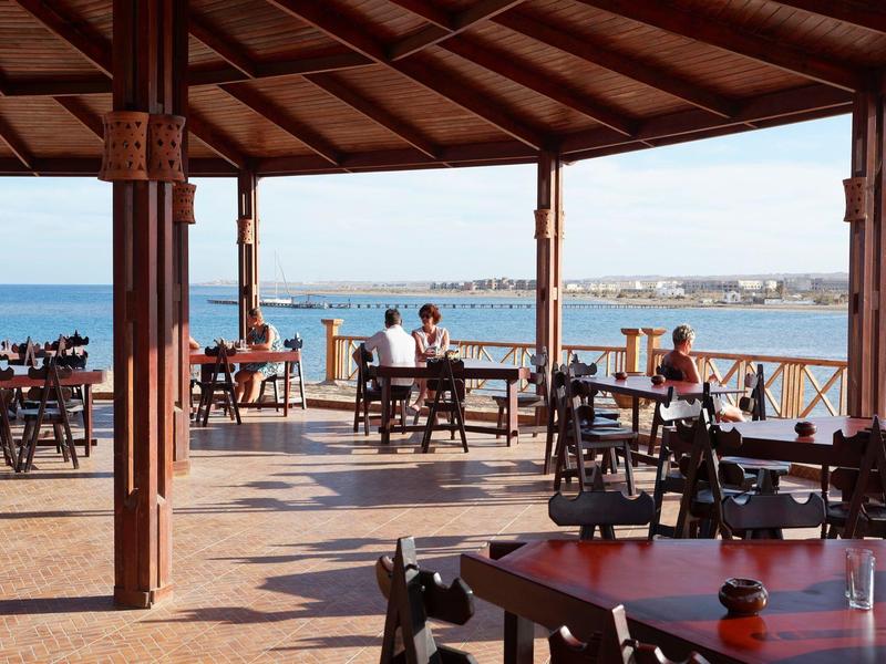 Terrazza del ristorante con vista sul mare, tavoli in legno e struttura aperta.