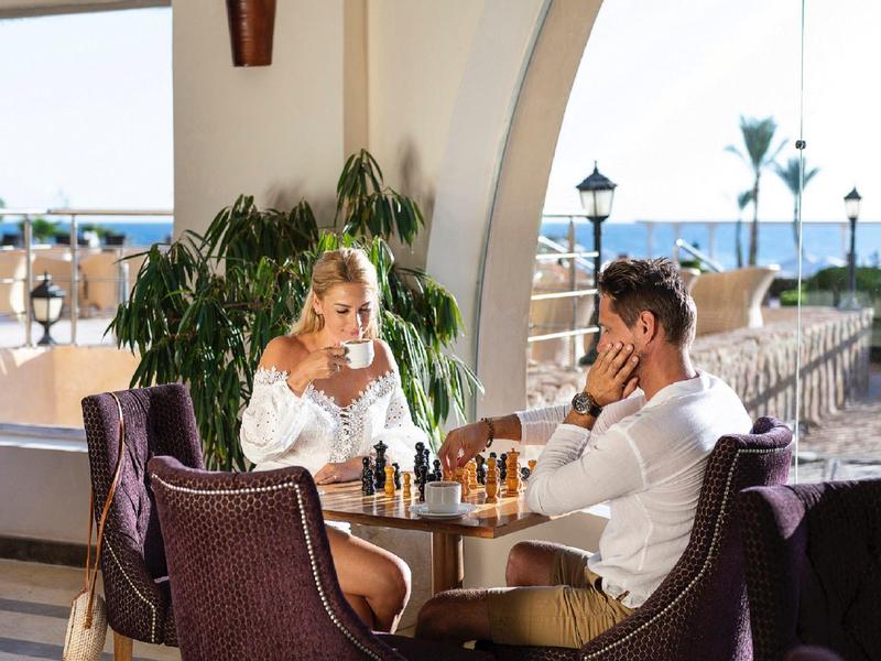 Coppia gioca a scacchi in un salone all'aperto con vista sul mare.