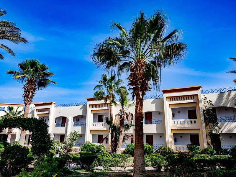 Hotelová budova s několika patry a palmami pod modrou oblohou.