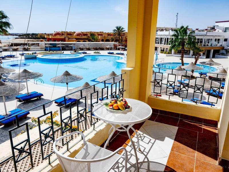 Balkon s stolem a židlemi s výhledem na bazén s lehátky a slunečníky v hotelu.