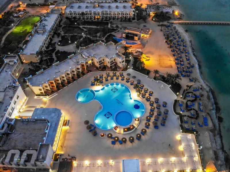 Noční pohled na osvětlený resort s bazénem a lehátky u moře.