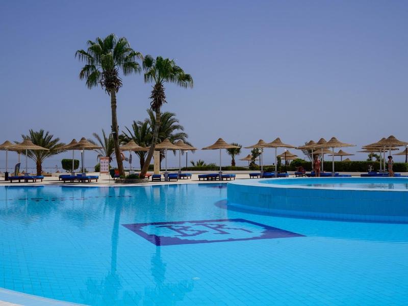 Velký bazén s čistou vodou, lehátky a palmami v hotelovém resortu pod jasnou oblohou