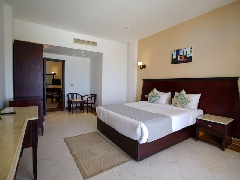 Světý hotelový pokoj s velkou postelí, dvěma křesly a psacím stolem v moderním stylu.