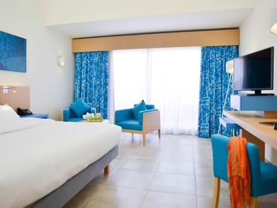 Bright hotel room with double bed, blue patterned curtains, and seating area by the window.